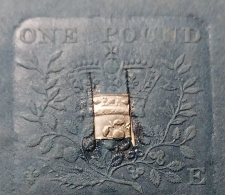 A silver one pound note featuring a crown and decorative foliage.