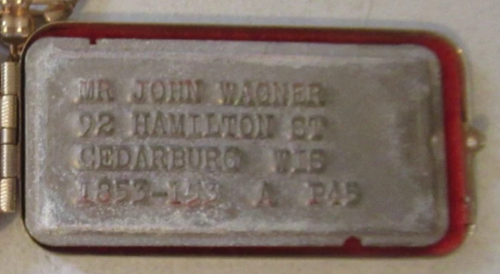 Metal identification tag with the name "Mr. John Wagner" and address details.