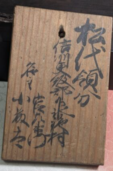 Wooden tag with handwritten Japanese text.